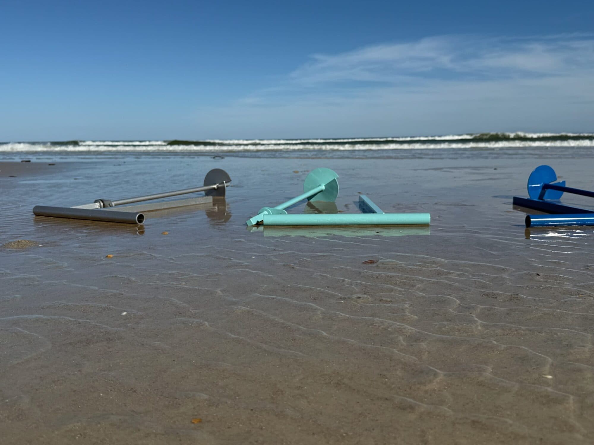 Iron Marine anchors at the water's edge, surf rolling in behind them
